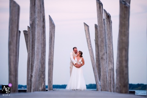 In Zeewolde, the Netherlands, a couple poses on a dock at sunset, framed artistically by the towering wooden pier pilons overhead for a dramatic portrait.