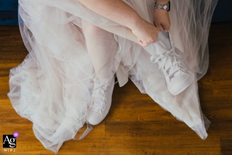 A high-angle detail shot in Nottinghamshire, East Midlands, captures the bride slipping her feet into a fresh pair of classic white wedding trainers at the couple's home.