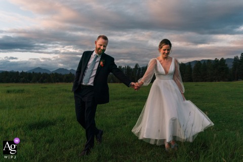 Double Arrow, Montana — The couple walks hand in hand through the grass at sunset, bathed in the soft, low light of a beautiful Montana evening for a romantic wedding portrait.