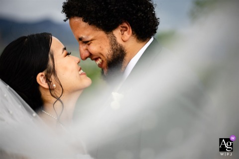The Pinery at The Hill, Colorado Springs, CO — The bride and groom giggle and smile together in a tight shot, wrapped in the bride’s flowing veil that sweeps around them, creating a joyful and intimate wedding portrait.