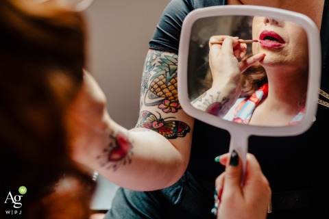A close-up detail at the Kimpton Clocktower Hotel in Manchester features a bride holding a mirror while a makeup artist precisely applies her lipstick for the ceremony.