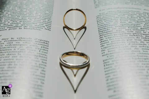 A pair of wedding bands, one gold and one silver, are placed on the open pages of a book, where their shadows artistically converge to form a heart shape during the wedding preparation details.