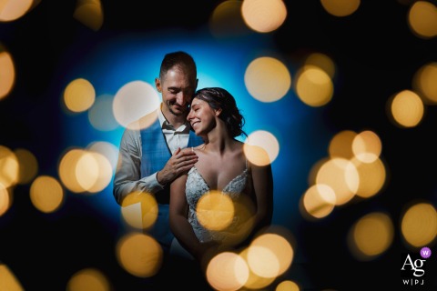 Abbaye des Prémontrés, Pont-à-Mousson, France — The newlyweds stand tenderly embraced and smiling, surrounded by large golden bokeh circles, with a blurred blue gradient backdrop creating a dreamlike and romantic wedding portrait at the ceremony location.