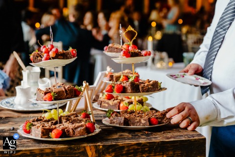 A wedding guest at Whitebottom Farm, Stockport, UK, reaches for a slice of cake on a beautifully textured table, capturing an artistic detail of the reception.