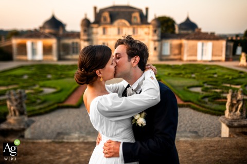 The couple shares a romantic kiss in front of the historic Château de Malle in Gironde, France, as the setting sun casts a warm glow over the estate.
