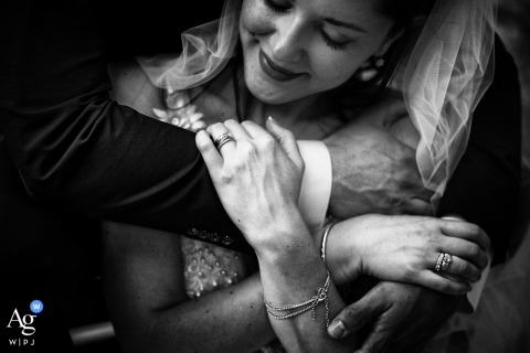 Lavagna Genova: A stylized close-up detail focuses on the groom's hand reaching toward the bride's shoulder, which she gently clasps, highlighting their new bond. 
