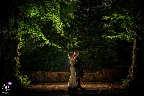 Sherbrooke Castle, Glasgow — The bride and groom are backlit by off-camera flash on a tree-lined road, with the trees dramatically rim-lit above them in a striking wedding portrait.