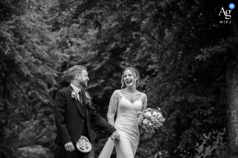 Sherbrooke Castle, Glasgow — The bride and groom share a laugh while walking in the venue grounds, captured in a black-and-white, semi-symmetrically framed wedding portrait.