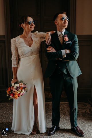 Chateau de Planchevienne — The stylish couple stands side by side indoors, both wearing sunglasses for a modern and chic wedding portrait at the château.
