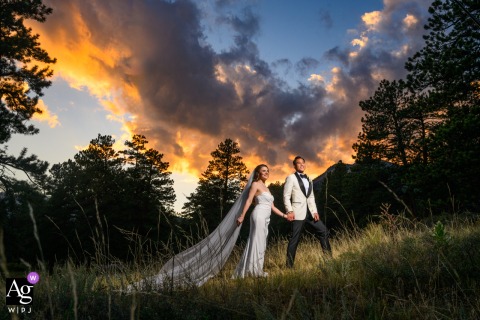 Fort Collins, Colorado — The bride and groom take a sunset stroll in the mountains near their reception location, dramatically lit by the photographer against a bold, colorful evening sky for a striking wedding portrait.