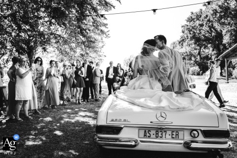 A vintage car carrying the embracing newlyweds arrives at Domaine de Cap'Bat, Landes, France, marking an artistic opening scene for the wedding celebration.