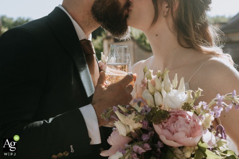 Celebrating their union with a toast, the bride and groom share a romantic kiss while holding glasses of champagne at Le Clos Barisseuse in France.