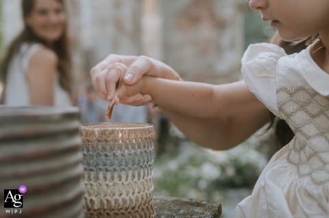 A close-up artistic detail created at Château du Vivier, France, shows the focused hands of a small girl intently holding a piece of paper as it burns in a quiet, symbolic moment.