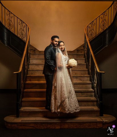 Elegant Timeless Wedding Portrait - Couple Embracing On Grand Staircase At Ballroom At The Ben Philadelphia Ballroom at the Ben, Philadelphia — The newlyweds share a timeless embrace with eyes closed on a grand staircase, symmetrically framed and bathed in golden light for a quiet and elegant wedding portrait.