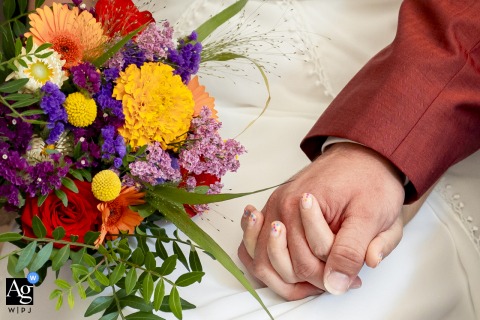 A tight artistic shot focuses on the subtle texture of the colorful wedding bouquet as a newly married couple gently clasps hands at the Mairie de Mens, Isère.
