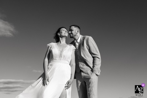 Auch, France — Under a vast sky, the groom is about to kiss the bride in a low-angle black and white portrait, creating a vintage-inspired and romantic wedding image.