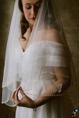 Harpswell, Maine — The bride holds up her veil before the wedding as a butterfly, symbolizing her late father’s memory, appears nearby in a tender and heartfelt getting ready portrait.