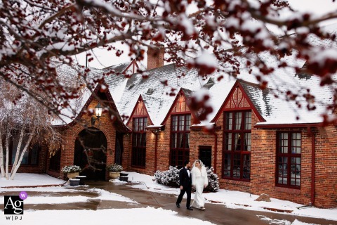 The bride and groom walk through the snowy courtyard at Wellshire Event Center, their figures framed by the softly illuminated architecture and snow-dusted trees, creating an artistic scene-setter of their Colorado wedding day.