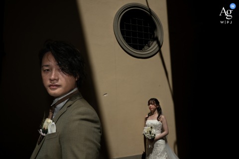 Florence, Tuscany — At their ceremony location, the bride enjoys a sun bath in the distance while the groom stands in the foreground, both bathed in warm light for an elegant wedding portrait.
