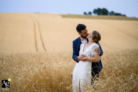 Toulouse, Haute-Garonne — The bride and groom share a kiss in a wheat field near the reception venue, captured in a minimalist, simple, and clean wedding portrait surrounded by open countryside.