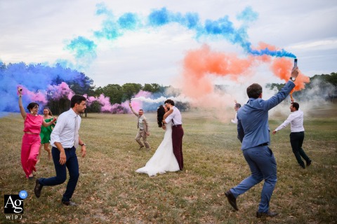 Château Flojague — The bride and groom kiss, surrounded by friends wielding colorful smoke bombs as the bridal party runs encircling them, creating a vibrant and dynamic wedding portrait.