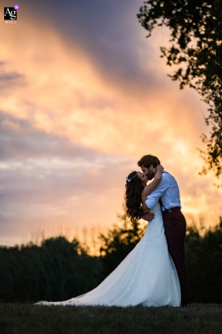Château Flojague — The bride and groom share a kiss at sunset, positioned low in a tall vertical frame, creating a romantic and elegant wedding portrait against the evening sky.