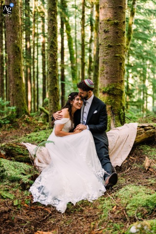 Sultan, WA — The bride and groom snuggle closely together on a downed tree trunk along the trail at their ceremony location, capturing a warm and intimate wedding portrait in the natural setting.