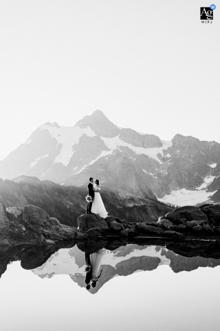 Mt. Baker, WA — At sunrise, the couple stands together above a reflective pond with an impressive, jagged mountain in the background, minutes before reciting their vows at the ceremony location.