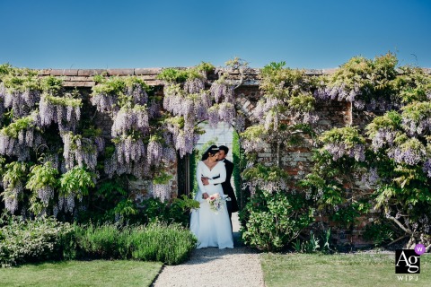 At North Cadbury Court Dorset Couple Stands Together Among Blooming Wisteria North Cadbury Court, Dorset — The couple stands together among blooming wisteria at North Cadbury Court, creating a romantic and colorful wedding portrait in the venue’s lush gardens.