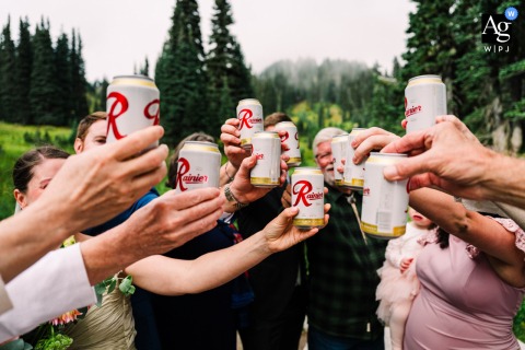 A detail-oriented wedding day artistic close-up from Mt. Rainier, WA, captures a pair of guests joyfully clinking their Rainier beer cans together immediately following the ceremony.