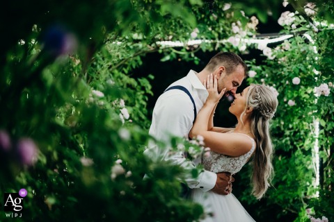 At Kingscote Barn Tetbury Bride and Groom Under Illuminated Rose Arch At Night Kingscote Barn, Tetbury — The bride and groom stand face to face under an illuminated rose arch at night, about to kiss, surrounded by lush green foliage in a romantic wedding portrait.