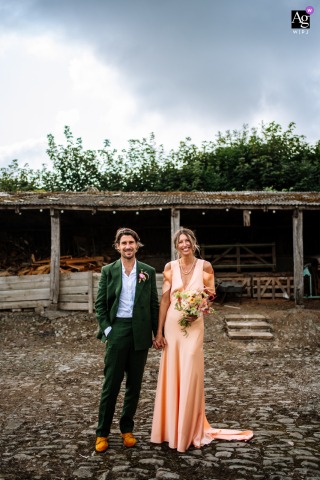 The Ash Barton Estate, Devon — The couple poses for a modern wedding portrait in the wood yard, centered and positioned low in the vertical frame, capturing the estate’s rustic atmosphere and contemporary style.