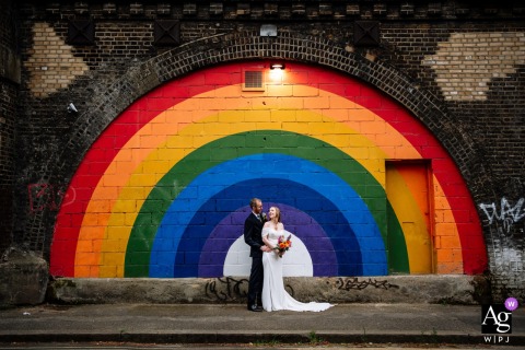 100 Barrington Road, Brixton — The couple poses for a portrait by the rainbow painting on a block wall, highlighting the vibrant urban art setting in Brixton for a colorful and creative wedding image.