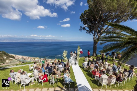 Villa Hamalia, Taormina Ceremony — A wide-angle scene captures the vibrant, saturated colors of the ceremony with an expansive vista, providing a picturesque overview of the wedding setting.