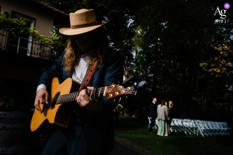Weingut Hahn, Alzey, Germany, shows a creative detail shot on the wedding day where the light casts a dramatic shadow across the guitarist's face as he plays, illuminating his guitar in the afternoon sunlight.