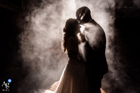 Kindergoed — The couple stands silhouetted in an old barn, sharing a backlit kiss as smoke surrounds them, creating an intimate and atmospheric wedding portrait at the venue.