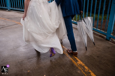 In Edmonton, Alberta, a creative artistic detail captures the bride and groom taking a romantic, with closed umbrellas in hand on their rainy wedding day at the reception location.