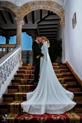 Castillo de Canena, Canena, Jaén, Spain — The couple stands illuminated on the stairs in a low-angle shot, creating a dramatic and elegant wedding portrait at the historic castle location.