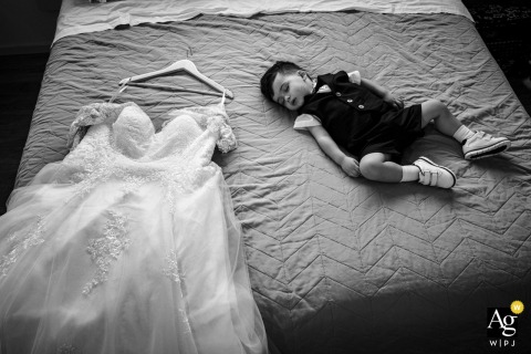 Ancona, Italy, a sleeping child rests peacefully next to the intricate lace and fabric of the bride's wedding dress, creating a quiet detail from the day.