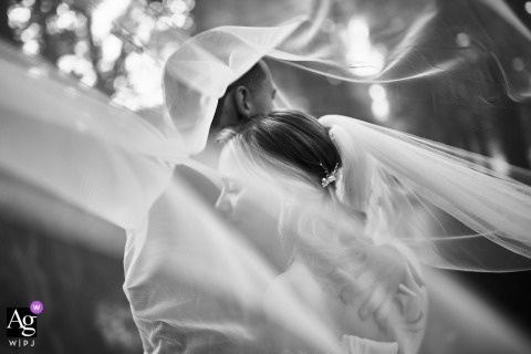 Noord Holland, In a park — The couple is captured in a black-and-white, dreamlike portrait as the wedding veil sweeps dramatically across both them and the frame, creating an artistic, obscured effect.