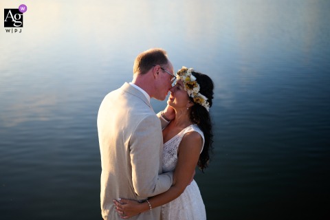 Amsterdam, Noord Holland — The couple is positioned low in the frame for a minimalist, symmetrical portrait near a lake, with a tranquil expanse of water creating a peaceful backdrop for their wedding image.