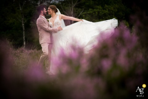 Rucphense Heide, Rucphen — The couple embraces among the purple moor flowers, with the bride playfully tossing her dress to the side, creating a vibrant and romantic wedding portrait in the natural setting.