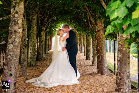 Rhinefield House Hotel — The couple shares a romantic kiss beneath a tree archway, framed by the trellis, capturing an intimate wedding portrait in the picturesque garden setting.