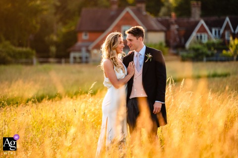 Couple Stands Together in Long Grass Golden Backlit Sunset Portrait Hampshire England Hampshire, England — In a golden, backlit sunset portrait at their parents’ house, the couple stands together in long grass, creating a warm and romantic wedding image in the countryside.