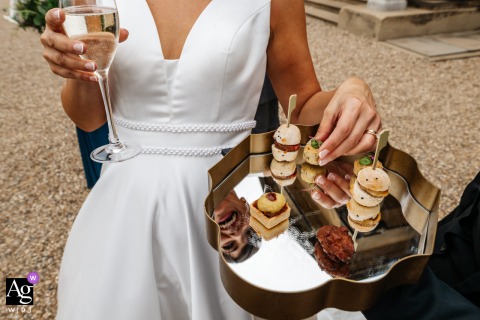 Rise Hall, Yorkshire, England - The bride, dressed in her wedding gown, reaches for a tray of canapés set against the elegant backdrop of the Rise Hall venue in Yorkshire, England, capturing a quiet, artful detail of the day.