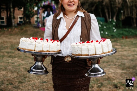 A server delivers two artfully designed wedding cakes to a reception area at Wolds Way Farm, Yorkshire, England, capturing the elegant details of the sweet centerpiece during the celebration.