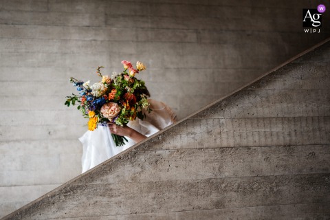 An elegant close-up showcases the bride's delicate bouquet as she descends the stone stairs of The National Theatre, London, England, highlighting the intricate details of the wedding day.