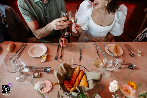 London, England: Inside the National Theatre, a creative detail image captures the bride and groom in a joyful toast as they clink sparkling champagne glasses together during their wedding day dinner celebration.