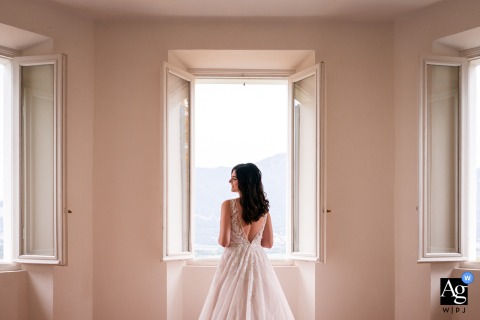 Villa Dolceacqua, Oggiono, Lake Como, Italy — The bride stands in front of a window, captured from behind as she turns her head to reveal her profile in a soft and elegant wedding portrait.
