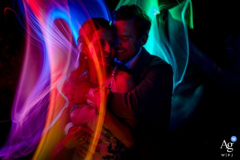 Sperlak Gallery, Cape May, NJ: Late-Night Dreamlike Embrace Amid Swirling Rainbow Lights Sperlak Gallery, Cape May, NJ — In a late-night, dreamlike portrait, the couple embrace amid swirling rainbow lights, creating an artistic and colorful atmosphere that highlights their connection in the gallery setting.
